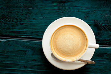 coffee with beautiful smooth froth in a classic white coffee cup top view on dark blue-green wooden table background