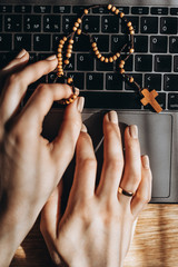 cropped view of woman hands using laptop and holding rosary beads at home