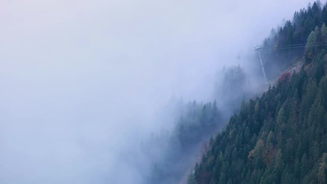 Cable car gondolas moving across the Alps mountain hill from misty cloud to the top. Autumn  misty morning view.  Picturesque traveling, seasonal, cloudy and misty weather condition background scene.