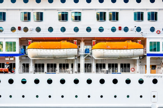 Closeup side view of a white passenger cruise ship with many round cabin windows and two lifeboats.