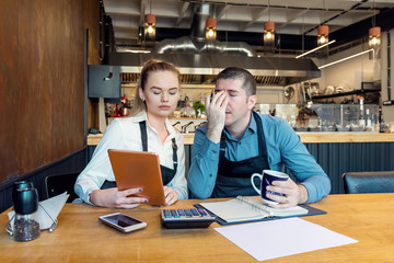 Worried business owners calculating finances - Small restaurant entrepreneurs SME go bankrupt due to Coronavirus pandemic - Young woman and man with headache and overwhelmed by financial difficulties