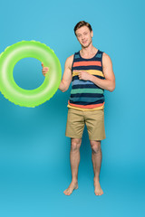 smiling man in striped singlet and shorts pointing with finger at swim ring on blue background