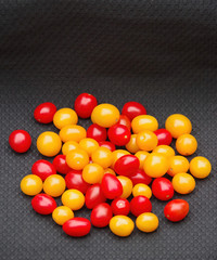 Close-up high angle view on a pile of tiny red and yellow sweet tomatoes on a black background