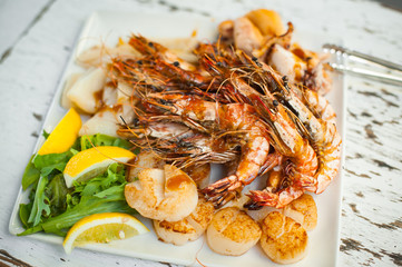 Saute shrimps, scallop, squid and lemon on white plate in the restaurant.