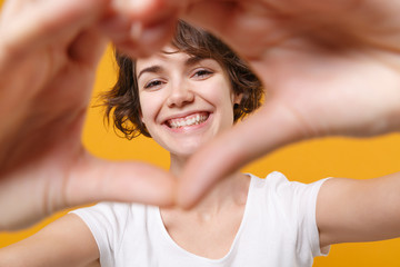 Smiling young brunette woman girl in white t-shirt posing isolated on yellow orange background in...