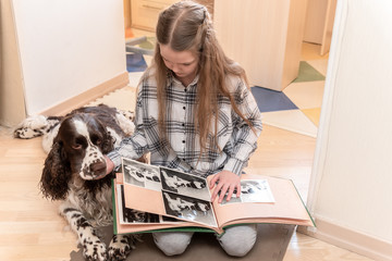 Young Cute girl looking photo album with her dog at home on floor.