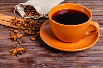 Cup of black aromatic coffee in a clay cup with anise stars and cinnamon sticks on a wooden background