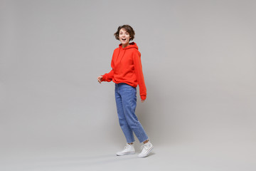 Side view of excited young brunette woman girl in casual red hoodie, blue jeans posing isolated on...