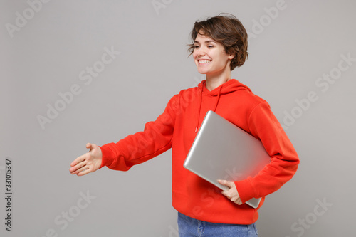 Smiling Young Brunette Woman In Casual Red Hoodie Posing Isolated On Grey Background People Lifestyle Concept Mock Up Copy Space Hold Laptop Pc Computer Stand With Outstretched Hand For Greeting Wall Mural Vidi Smiling Young Brunette Woman In Casual Red Hoodie Posing Isolated On Grey Background People Lifestyle Concept Mock Up Copy Space Hold Laptop Pc Computer Stand With Outstretched Hand For Greeting Wall Mural Vidi