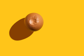Brown cracked chicken egg on a bright yellow background with copy space. Top view. Minimal food concept