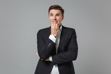 Nervous shocked young business man in classic black suit shirt posing isolated on grey background in studio. Achievement career wealth business concept. Mock up copy space. Put hand prop up on chin.