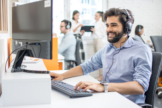 Smiling friendly helpline technical support agent with hands-free headset at call centre.