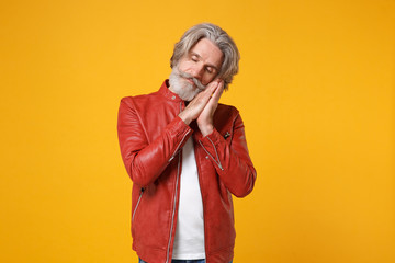 Relaxed elderly gray-haired mustache bearded man in red leather jacket isolated on yellow orange wall background. People lifestyle concept. Mock up copy space. Sleep with folded hands under cheek.