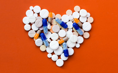 Heap of white pills, tablets in shape of heart, capsules on red orange background. Drug prescription for treatment medication health care concept wth copy space.