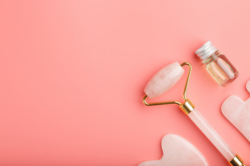 Gua sha massage tool made of natural pink Quartz-roller, jade stone and oil, on a pink background for face and body care. Part of traditional Chinese medicine