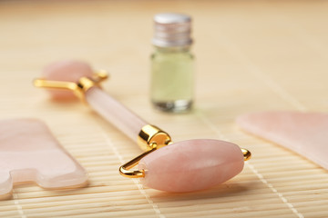 Gua sha massage made of natural rose Quartz-roller, jade stone and oil, on a bamboo background for face and body care.