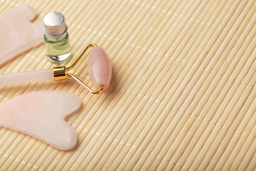 Fototapeta na wymiar Gua sha massage made of natural rose Quartz-roller, jade stone and oil, on a bamboo background for face and body care.