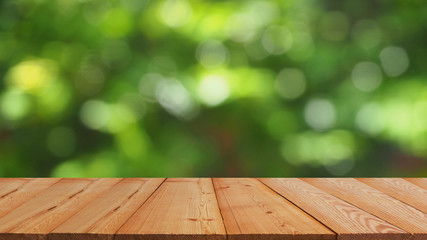 brown wood plank table top on blur and bokeh abstract green tree in the gardening for banner design or natural display product background with copy space.