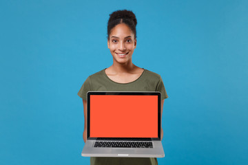 Smiling young african american woman girl in casual t-shirt posing isolated on blue background in studio. People lifestyle concept. Mock up copy space. Hold laptop pc computer with blank empty screen.