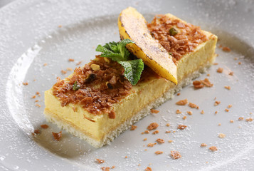 Desserts. Fruit cake with sponge cake and yellow mousse. Mint, yellow slice and powdered sugar on a light plate. Copy space