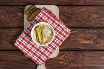 A plate of mashed potato with steamed cutlet and pickled cucumbers on a wooden background .