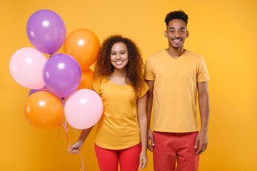 Smiling young friends couple african american guy girl in casual clothes isolated on yellow orange background. Birthday holiday party, people emotions concept. Celebrating hold colorful air balloons.