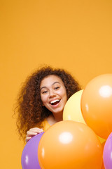 Cheerful young african american girl in casual clothes isolated on yellow orange background. Birthday holiday party people emotions concept. Mock up copy space. Celebrating hold colorful air balloons.