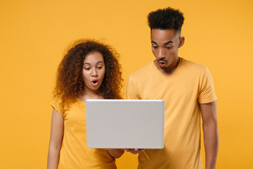 Shocked young friends couple african american guy girl in casual clothes isolated on yellow orange...