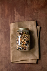Obraz na płótnie Canvas Homemade crunchy puffed millet grain granola with dried fruits and nuts in glass maison jar on textile napkin over brown texture background. Flat lay, space. Healthy food eco friendly breakfast