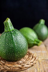 Close-up of three round zucchini with selective focus, on rustic wooden board, vertical black background