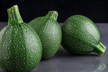 Close-up of three round zucchini on dark gray background, with selective focus and black background, horizontal