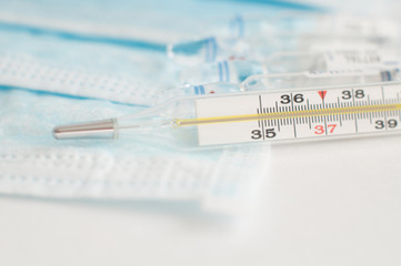 Sterile medical blue masks, vials with vaccine and analogue thermometer on white background.