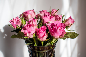 Bouquet of fresh delicate light pink roses and blurred green leaves in a vase in a sunny summer day, beautiful indoor floral background photographed with soft focus
