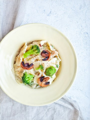Farfalle with broccoli, chicken fillet and mushrooms in cream sauce on a light background top view. Pasta with cheese and pepper.