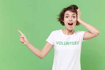 Shocked young woman in white volunteer t-shirt isolated on pastel green background. Voluntary free...