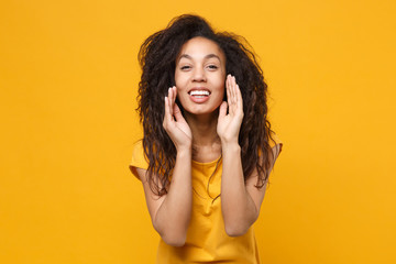 Cheerful young african american woman girl casual t-shirt posing isolated on yellow orange background in studio. People lifestyle concept. Mock up copy space. Screaming with hands gesture near mouth.