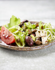 Healthy salad with feta cheese, various olives, leek and tomatoes. Bright wooden background. Close...