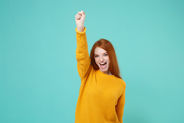 Cheerful young redhead woman girl in yellow sweater posing isolated on blue turquoise wall...