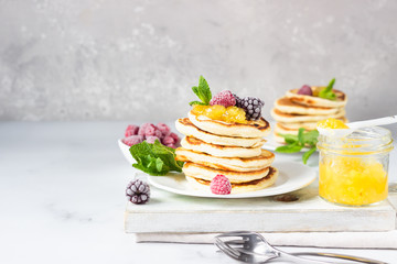 Homemade pancakes with jam, frozen raspberries and blackberries and mint on wooden cutting board. Light grey background. Breakfast. 
