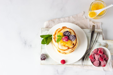 Homemade pancakes with jam, frozen raspberries and blackberries and mint on wooden cutting board. Light grey background. Breakfast. Top view. 
