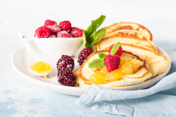 Pancakes with orange jam, frozen berries (raspberries and blackberries) and mint on light blue stone background. Breakfast. 