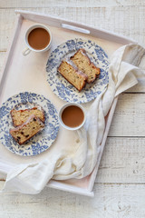 Home baked banana cake with chocolate drops and two coffee cups on a white tray