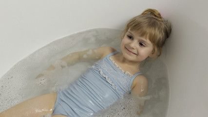 Cute blonde girl takes a bath in swimwear. Little child, 4 years old. Hygiene
