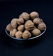bowl of walnuts steel plate black background close up