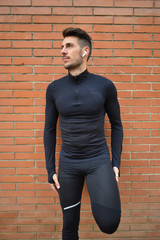 Hombre joven y deportivo, escuchando música con unos cascos blancos, vistiendo un conjunto negro...