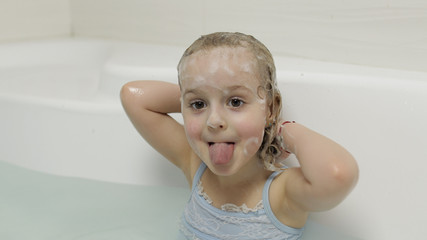 Cute blonde girl takes a bath in swimwear. Little child washes her head