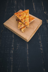 Some pieces of meat pie on kitchen cutting board on black wooden background. Tasty healthy food. Diet, nutrition, eating habits concept. Place for text. Vertical shot.