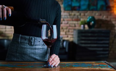 Woman pouring red wine into wine glass.