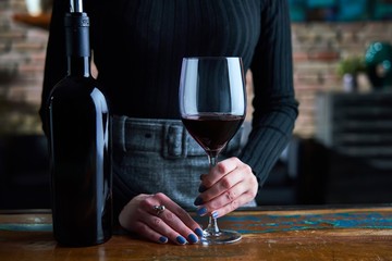 Woman tasting red wine, holding wine glass.