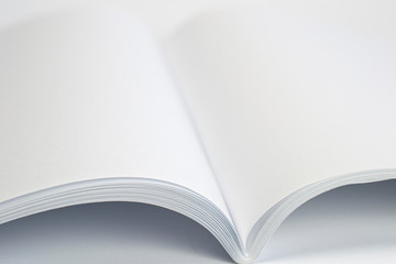 Opened blank magazine with white pages on white background and close-up selective view.